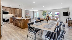 Une cuisine moderne avec des meubles en bois, un îlot central et un coin repas comprenant des chaises en cuir noir et une table en bois.