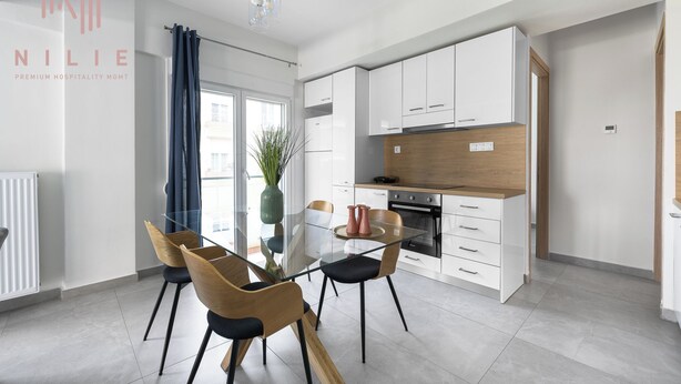 Une cuisine moderne avec des meubles blancs, un plan de travail en bois et une table à manger en verre, accompagnée de chaises.