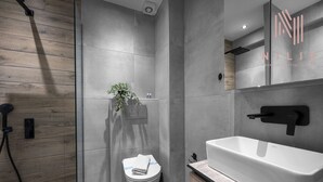 Une salle de bain moderne avec un plancher en bois, des toilettes blanches, une grande baignoire blanche et un lavabo fixé au mur.