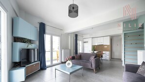 Un salon moderne avec un canapé, une table basse et un meuble pour la télévision. On aperçoit un coin cuisine au fond.