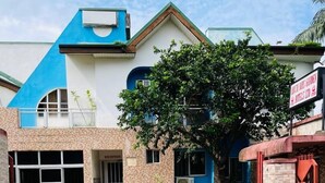 A gated entrance to a building with a reception desk, a tree in the foreground, and a sign for a hotel. - Abuja Bays Garden Hotel (Abuja)