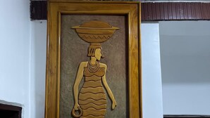 A framed artwork of a woman carrying a pot on her head, mounted on a white wall. - Abuja Bays Garden Hotel (Abuja)