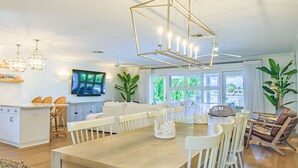A spacious living area with a wooden dining table, white chairs, and a modern chandelier. - ☀️Private Home with Pool/Hot Tub🌊Water Views 🌴Outdoor Kitchen🐬Private Dock (Indian Rocks Beach)
