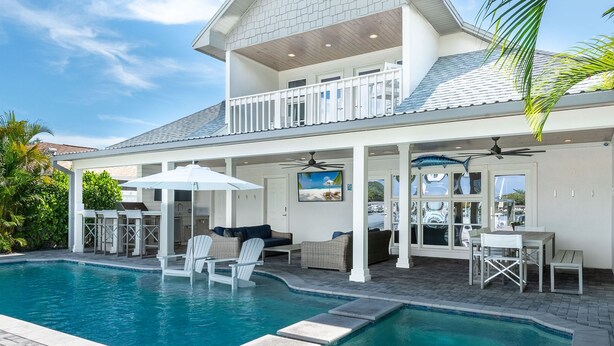A two-story house with a swimming pool, outdoor seating, and a balcony. - ☀️Private Home with Pool/Hot Tub🌊Water Views 🌴Outdoor Kitchen🐬Private Dock (Indian Rocks Beach)