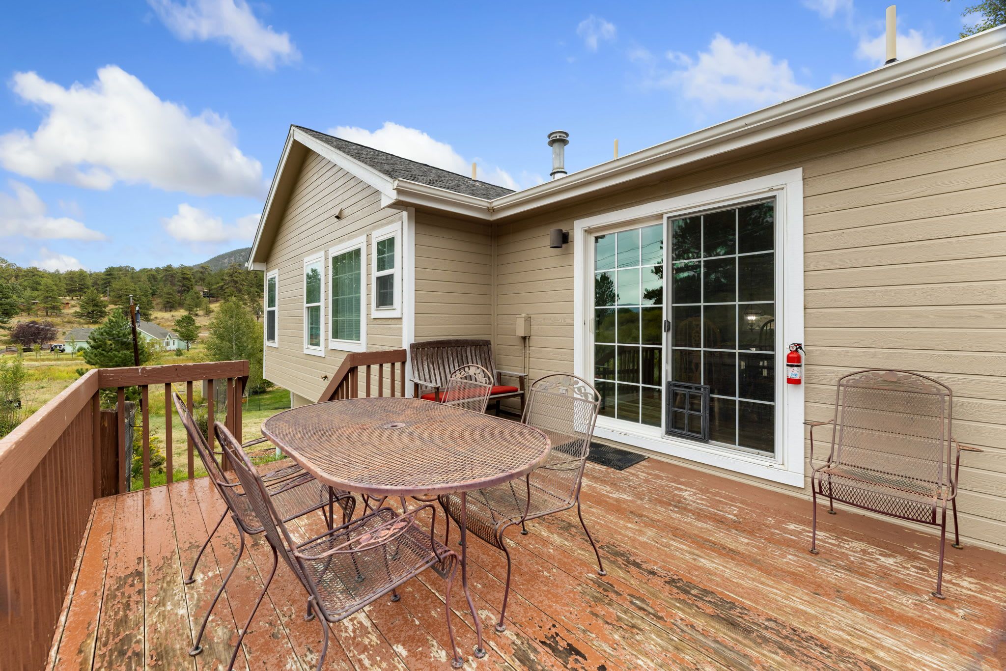 A deck with a metal table and chairs, a wooden bench, and a sliding glass door leading to a covered porch.