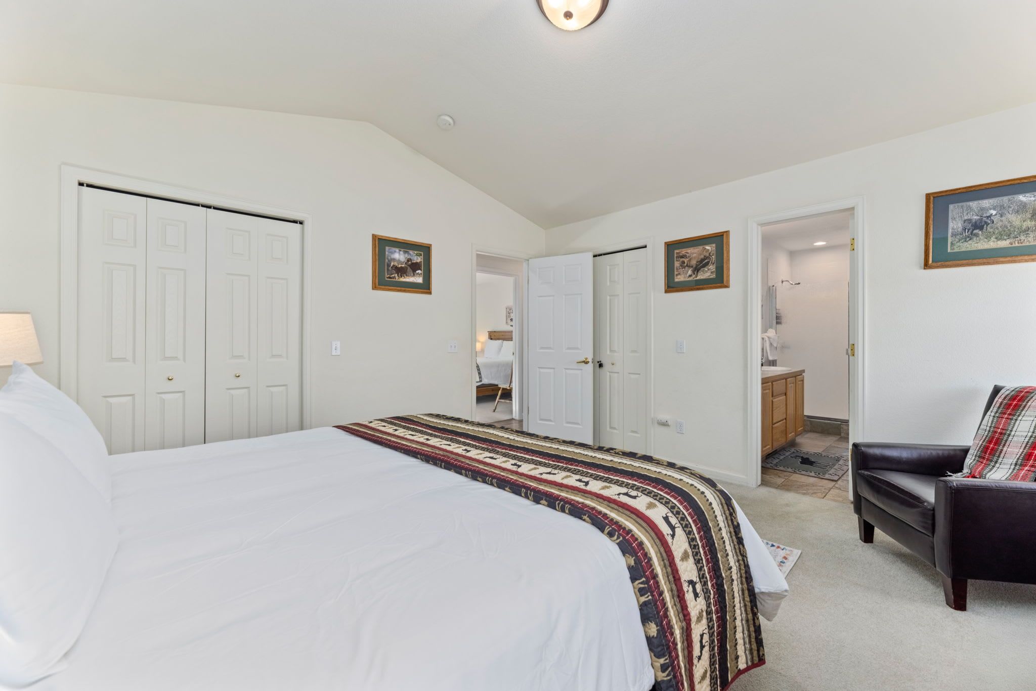 Une chambre avec un grand lit, une chaise et un bureau. Il y a deux portes, l’une donnant sur une salle de bain et l’autre sur une cuisine.