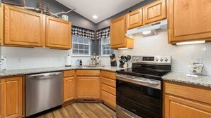 Une cuisine avec des meubles en bois, un lave-vaisselle, un four et une fenêtre ornée de rideaux à carreaux.