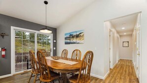 Un coin repas avec une table et des chaises en bois, un luminaire suspendu et une vue sur une terrasse extérieure, accessible par une porte vitrée.