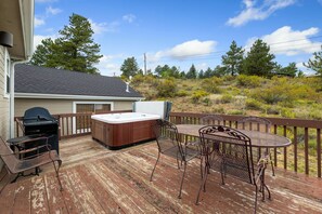 Une terrasse en bois avec un jacuzzi, un barbecue, ainsi qu’une table et des chaises en métal.