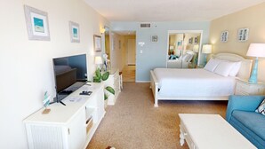 A hotel room with a bed, a desk with a TV, a chair, and a small table.