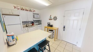 Cocina compacta con armarios blancos, microondas, cafetera y tostadora sobre la encimera.
