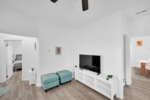 Relax in this stylish living room with a large flat-screen TV, comfortable seating, and a touch of greenery.