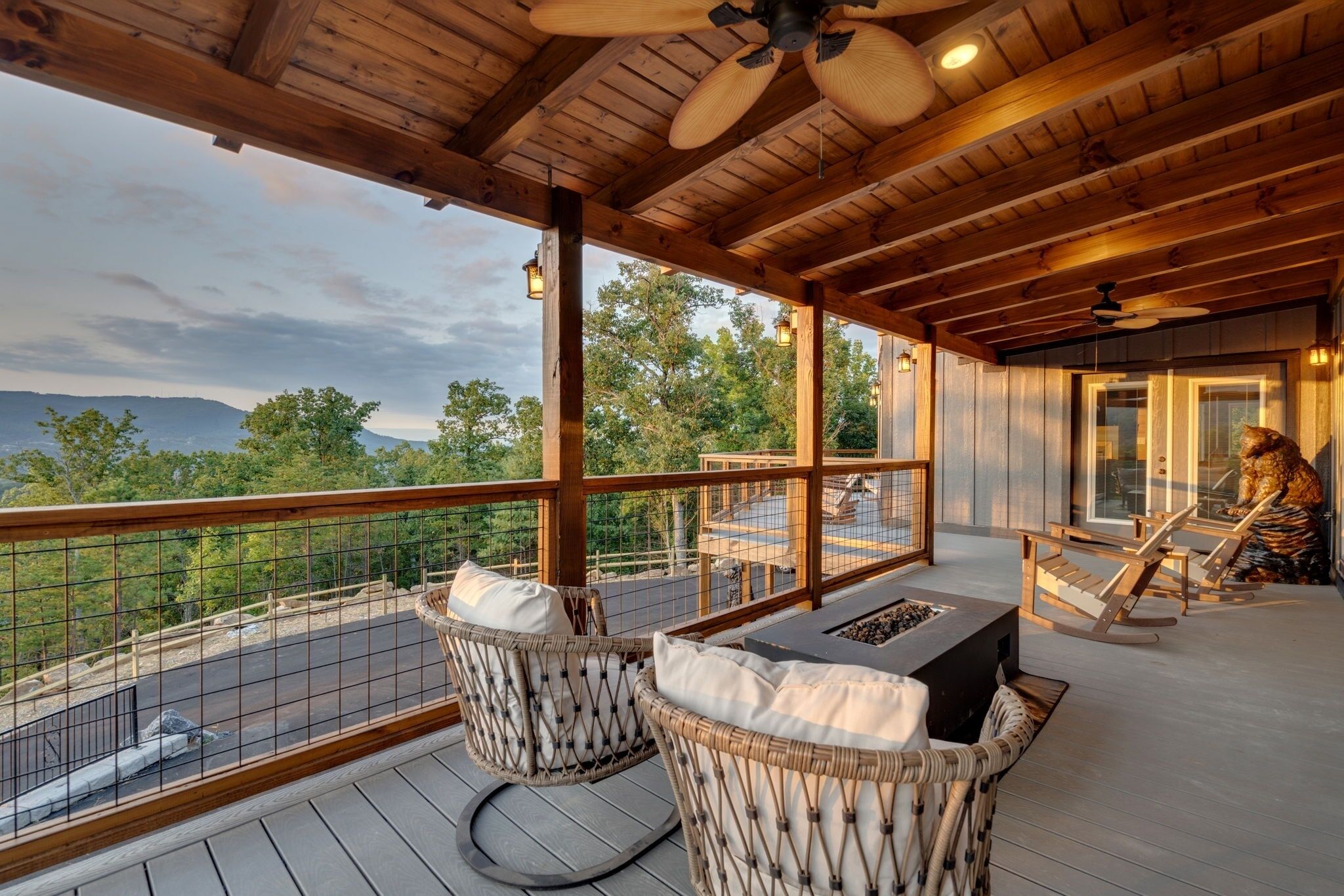 A wooden deck with wicker chairs and a table, overlooking a scenic landscape.
