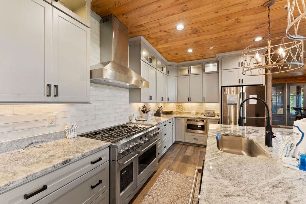 A modern kitchen with stainless steel appliances, white cabinetry, and a wooden ceiling.