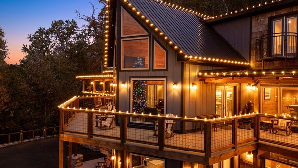 A two-story wooden house with a balcony and deck, decorated with string lights.