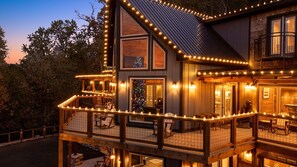 Une maison en bois à deux étages, dotée d’un balcon et d’une terrasse, décorée de guirlandes lumineuses.