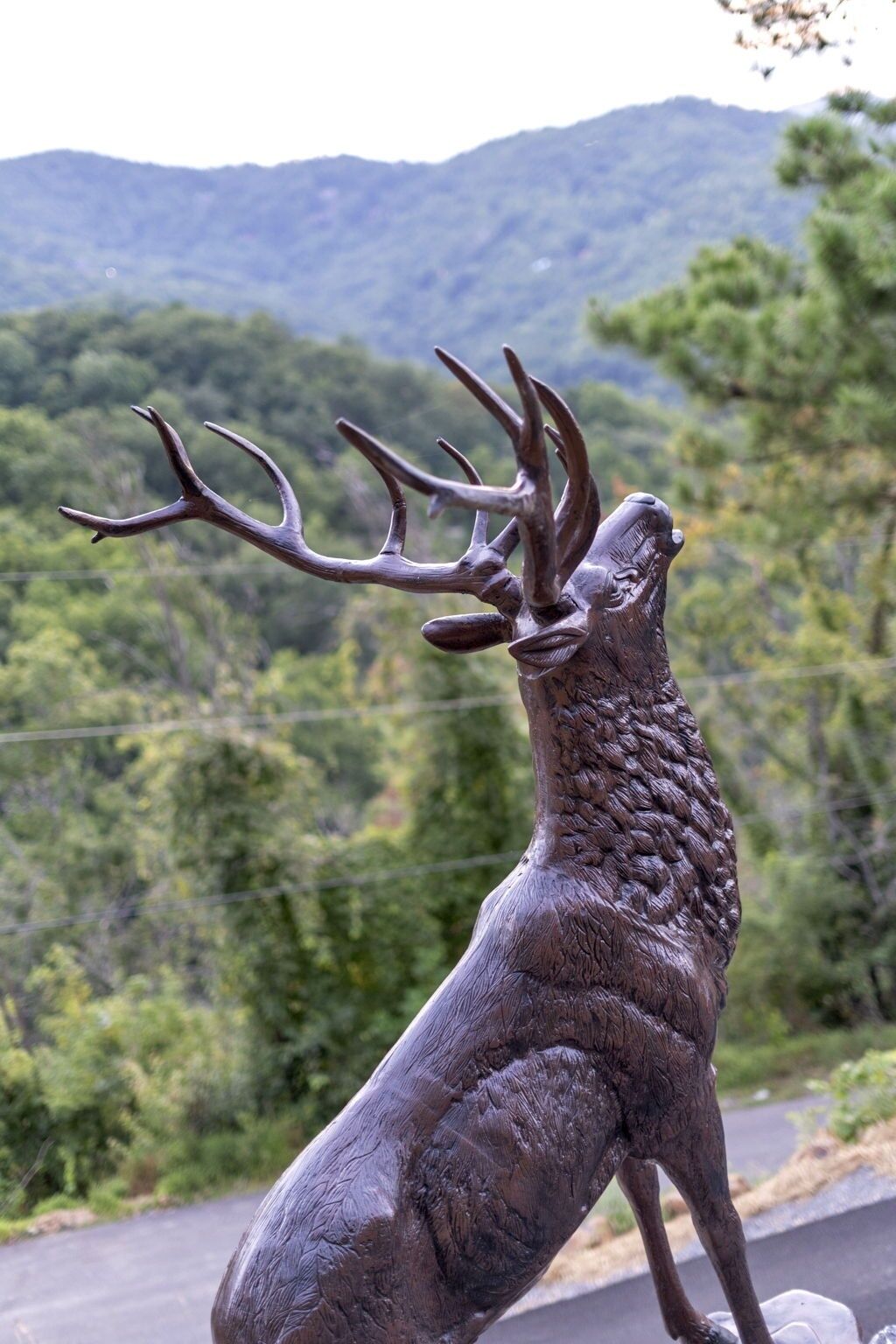 Une sculpture de cerf, avec ses bois, placée sur un fond représentant une forêt et des montagnes.