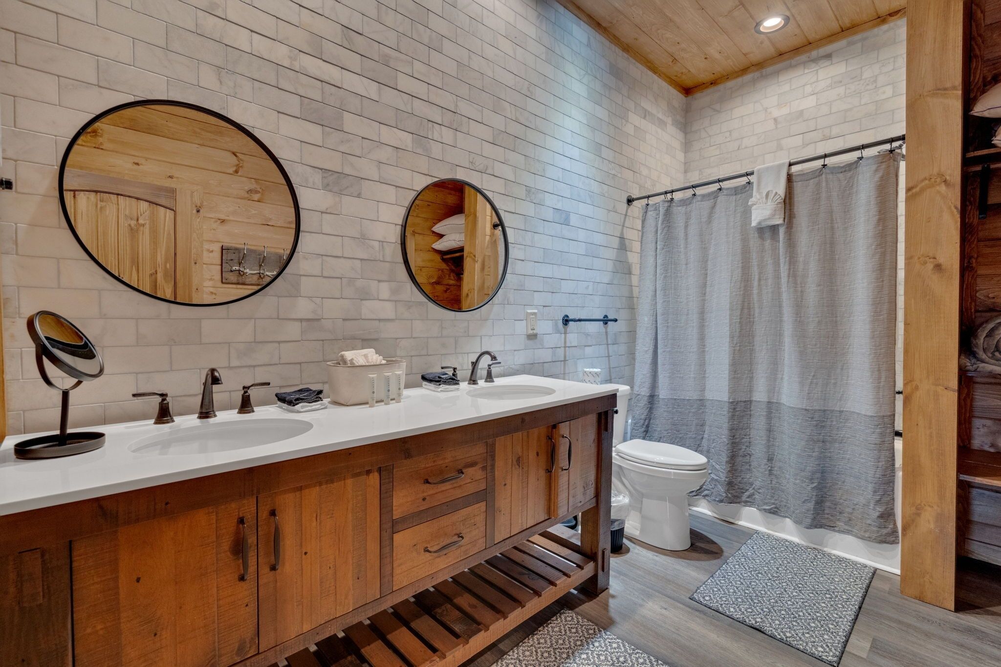 Une salle de bain avec un meuble-lavabo en bois, deux vasques, des toilettes et un rideau de douche.