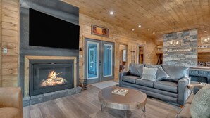 A cozy living room with a fireplace, a large flat-screen TV, a stone accent wall, and a comfortable seating area.