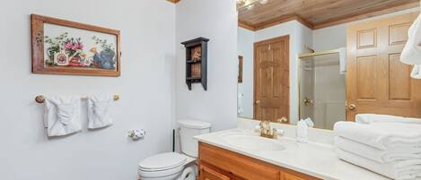 Un baño con tocador de madera, un espejo grande, un inodoro y una obra de arte floral enmarcada en la pared.
