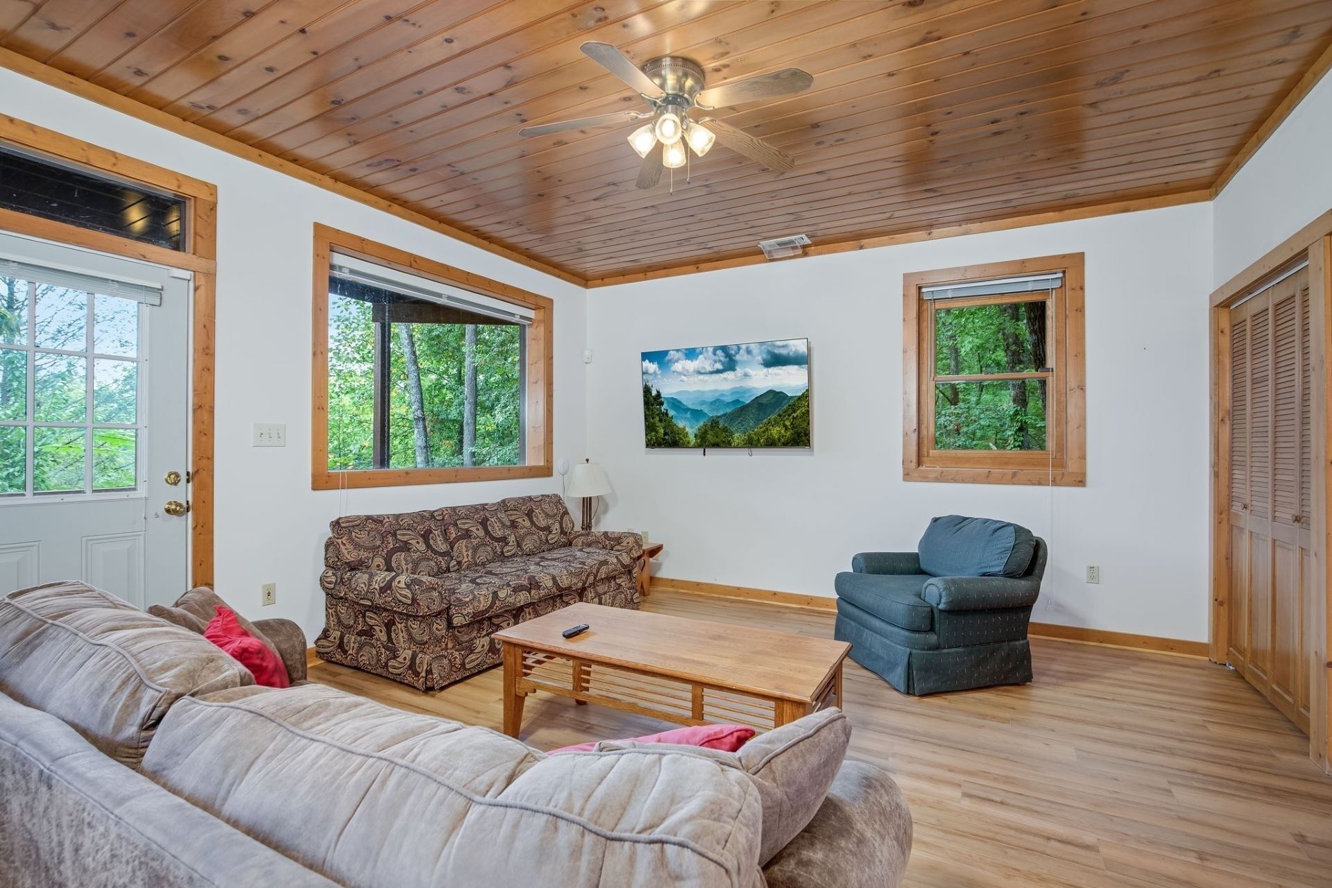 A cozy living room with a wooden ceiling, a sofa, a chair, and a painting of a mountain landscape.