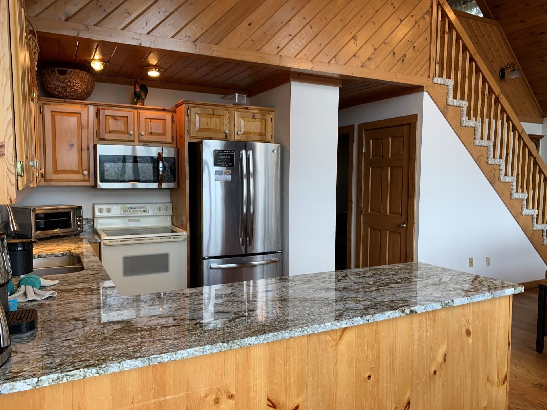 A kitchen with wooden cabinets, a stainless steel refrigerator, a microwave, a stove, and a granite countertop.