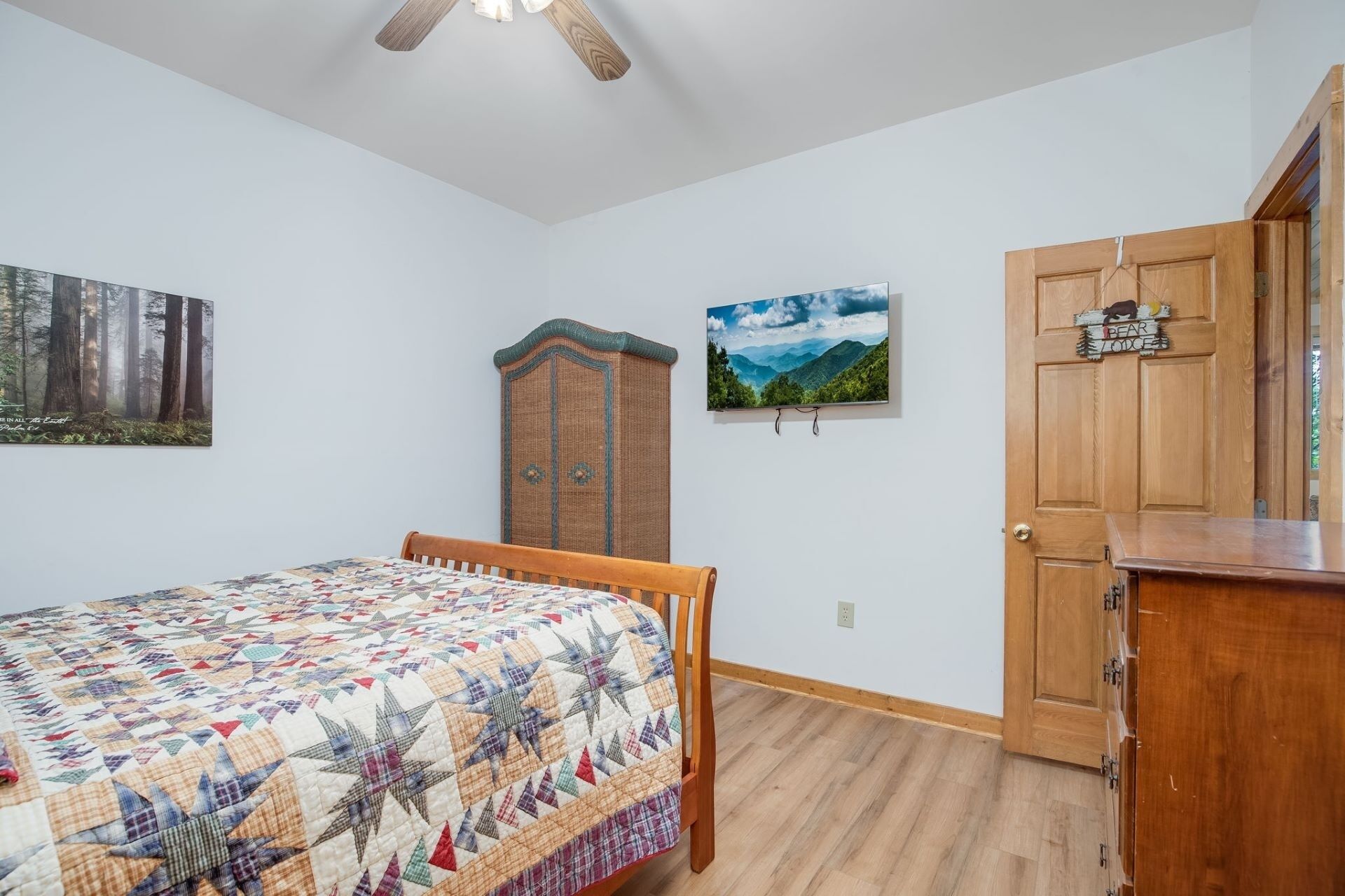 A bedroom with a wooden bed, a wooden wardrobe, a door with a bear decoration, and two framed pictures on the wall.