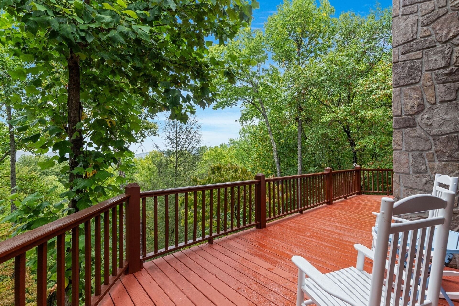 A wooden deck with a stone wall, surrounded by lush greenery and trees.