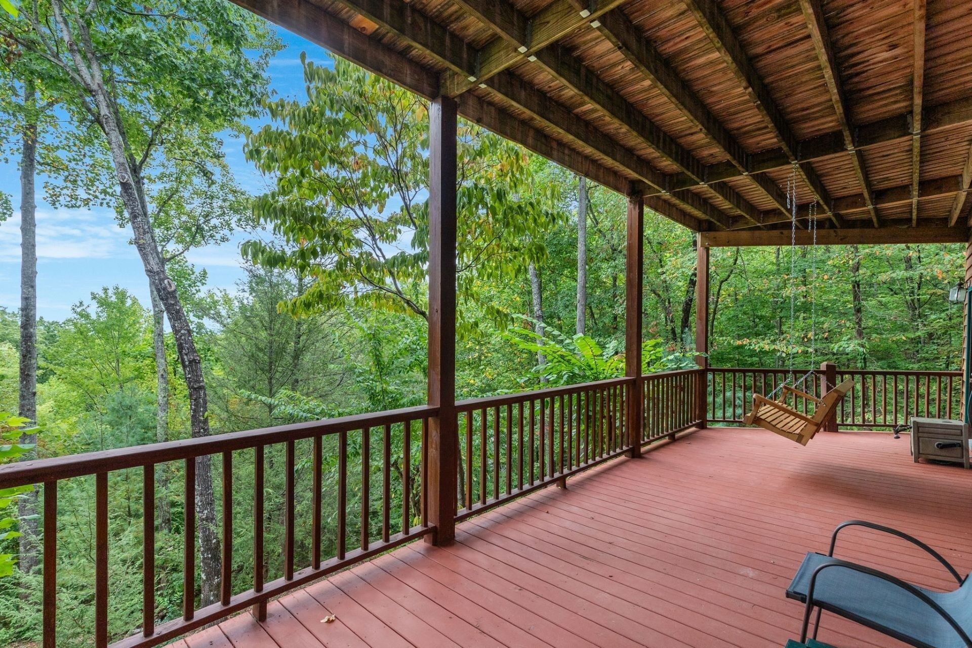 A covered outdoor deck with a swing chair and a bench, overlooking a forested area.