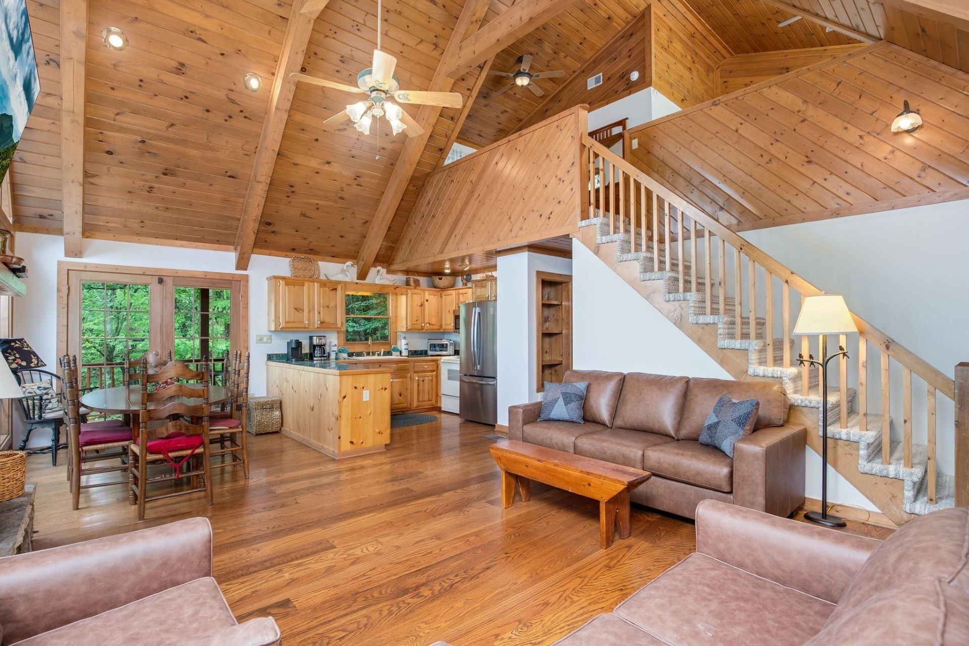 A spacious living area with a wooden ceiling, a staircase, and a kitchen in the background.