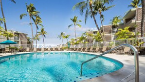 A swimming pool with a metal handrail, surrounded by lounge chairs and palm trees, with a clear blue sky in the background. - Big Island Ali'i Villas 333 2 Bedroom Condo (Kailua-Kona)