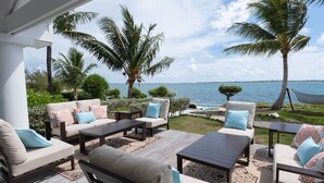 An outdoor patio with seating, palm trees, and a view of the sea. - Middle Cay Estate 7 Bedroom Estate (Middle Cay)