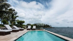 A rectangular swimming pool with clear blue water, surrounded by lounge chairs and wicker furniture. - Middle Cay Estate 7 Bedroom Estate (Middle Cay)