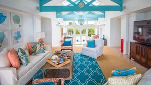 A spacious living room with a high ceiling, white sofas, blue accents, and a large TV. - Middle Cay Estate 7 Bedroom Estate (Middle Cay)