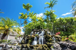 A waterfall cascading over rocks with lush greenery and palm trees in the background. - Budget Luxury, Grand Champion Golf Villa #129 - 2 Bd/2 Bath-NEW upgrades! (Wailea)