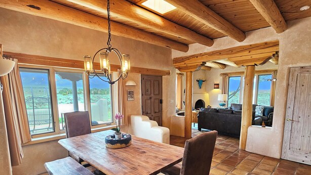 Un interior rústico con una mesa de comedor de madera, bancos y una araña.