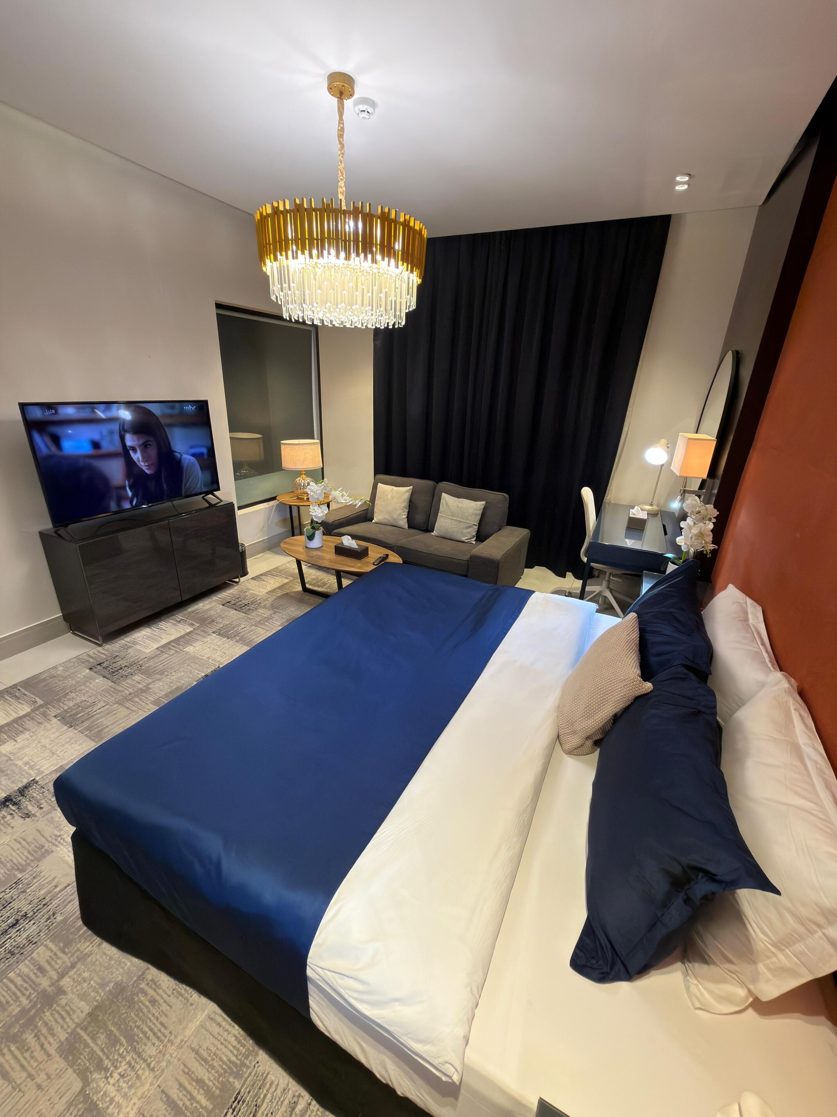 Een hotelkamer met een bed, een televisie, een bank, een bureau met een lamp en een grote spiegel.