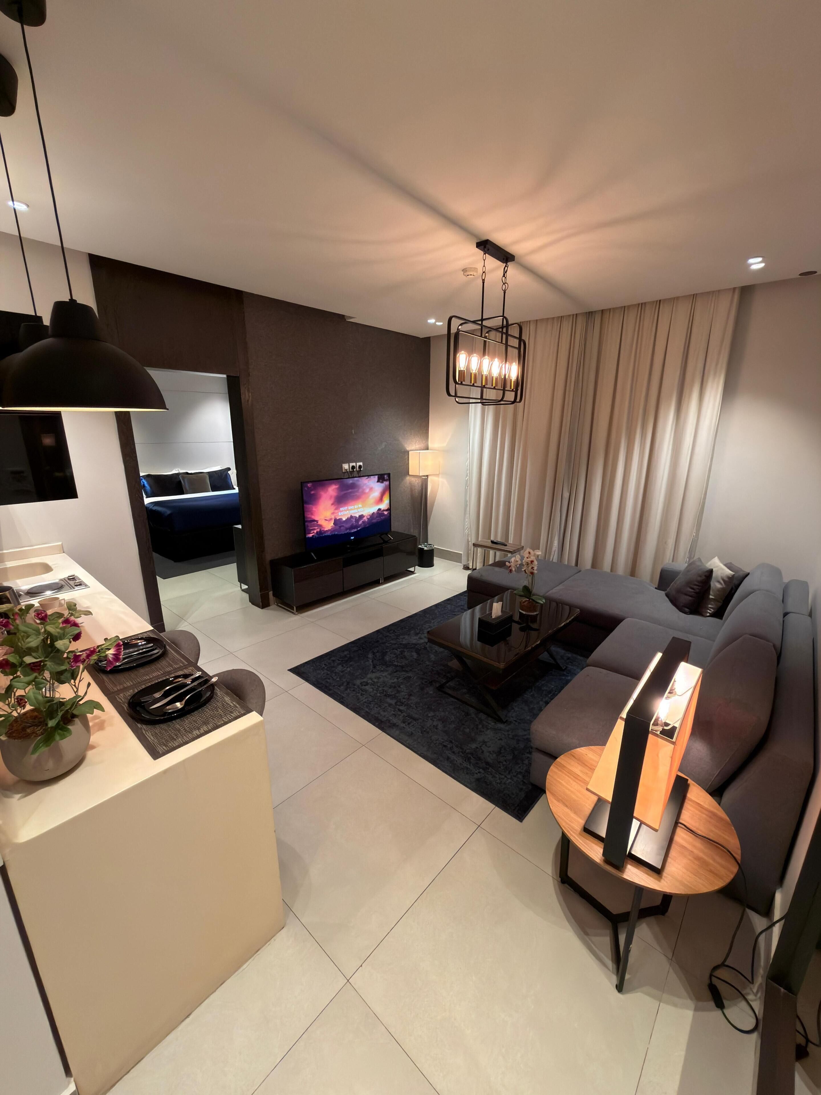 Una sala de estar moderna con un sofá, una mesa de centro y un televisor. Hay un comedor con una mesa dispuesta para dos personas.