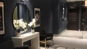 Ένας μοντέρνος εσωτερικός χώρος με έναν πάγκο υποδοχής, δύο μαύρες καρέκλες, έναν στρογγυλό καθρέφτη και ένα δάπεδο με σχέδια.