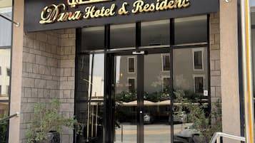 La entrada al Dana Hotel & Residences con un toldo negro, puertas de cristal y una alfombra roja que conduce a la entrada.