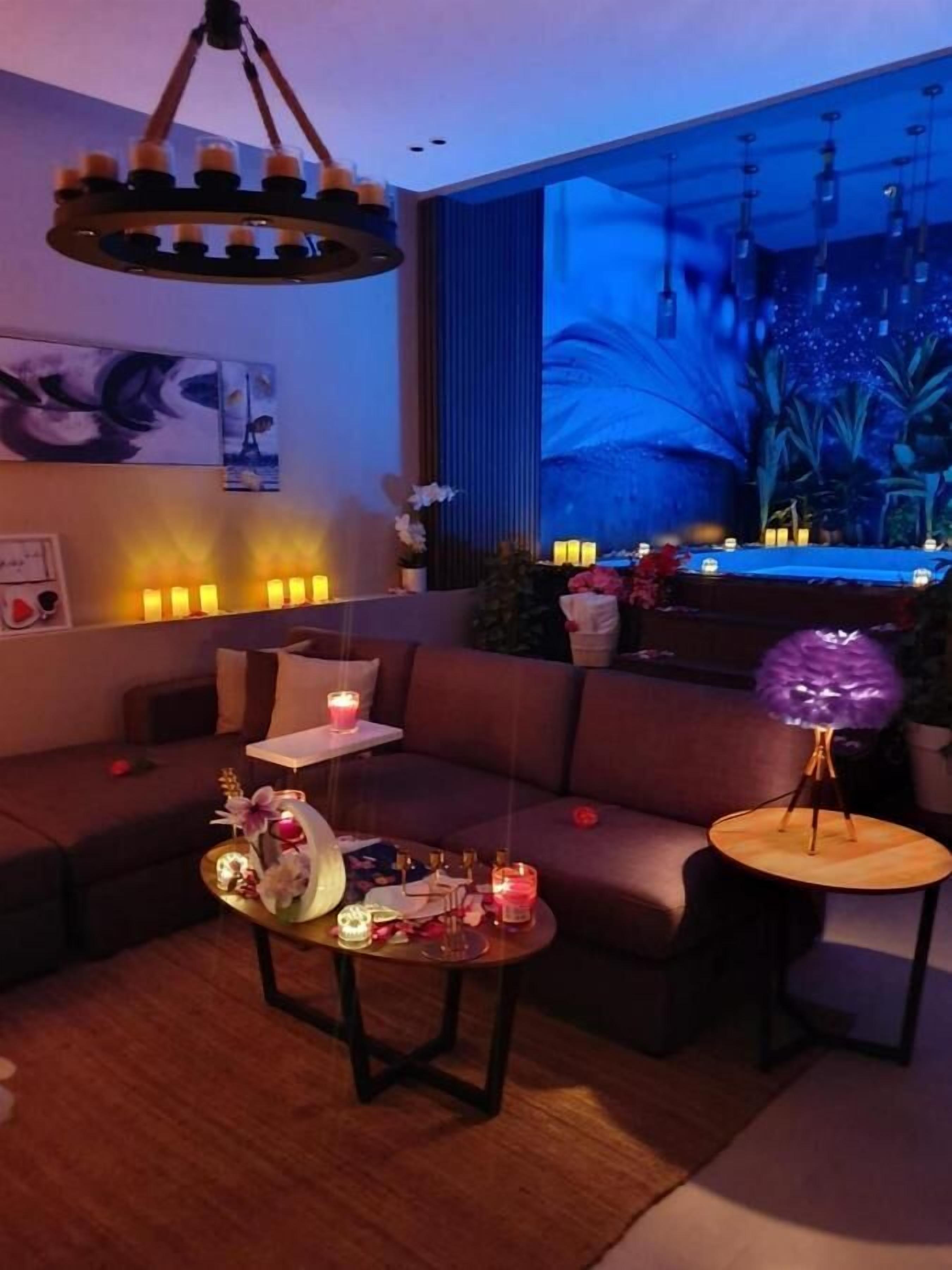 A modern living room with a sofa, a coffee table with candles, and a large window with a view of a garden.