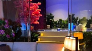 Ένα μοντέρνο σαλόνι με έναν καναπέ, ένα τραπεζάκι σαλονιού με κεριά και ένα μεγάλο παράθυρο με θέα σε έναν κήπο.