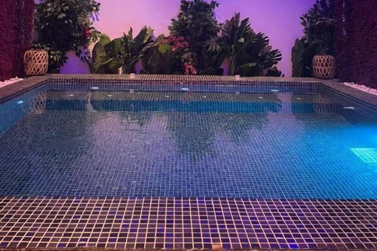 An indoor swimming pool with a tiled floor and walls, surrounded by lush plants and decorative vases.
