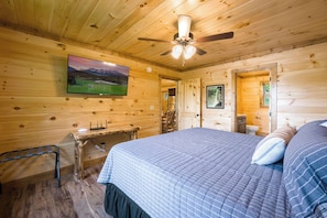 A wooden cabin room with a bed, a desk, a television, and a ceiling fan. - 4/4 Cabin w 4 King Suites|Hot Tub|Views 5 min to Gatlinburg! (Gatlinburg)