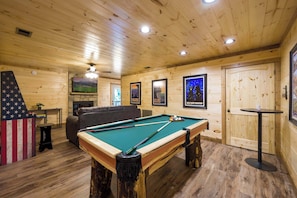 A pool table in a wooden room with a sofa, a small table, and a TV mounted on the wall. - 4/4 Cabin w 4 King Suites|Hot Tub|Views 5 min to Gatlinburg! (Gatlinburg)