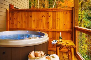 Una terraza de madera con un jacuzzi, una mesa con una botella y un vaso, y toallas.