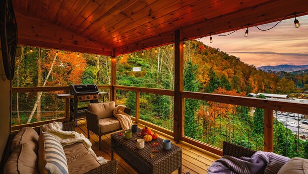 A wooden deck with a sofa, chairs, and a table with pumpkins and mugs. - 4/4 Cabin w 4 King Suites|Hot Tub|Views 5 min to Gatlinburg! (Gatlinburg)