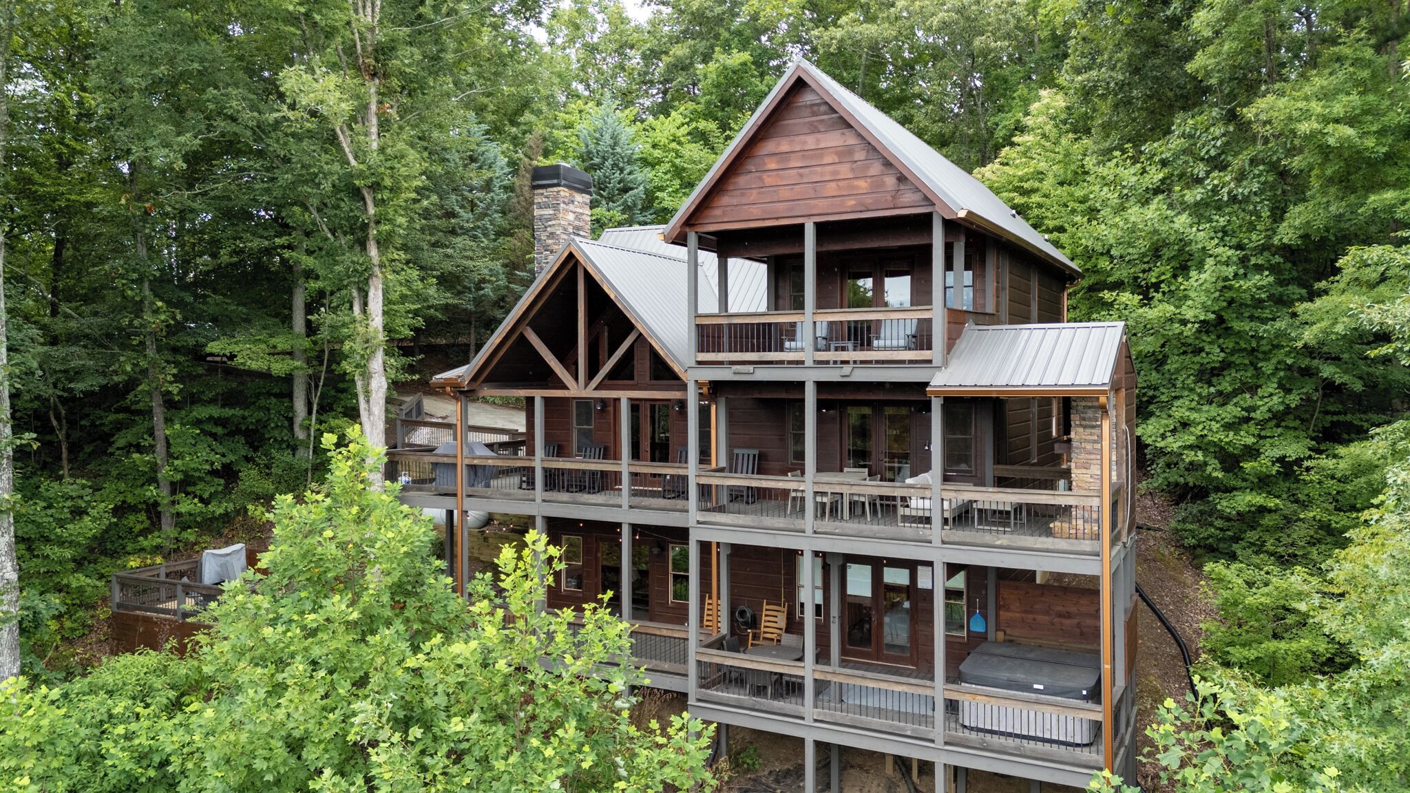 Une cabane en bois à plusieurs étages, dotée de balcons et entourée d’une forêt dense.