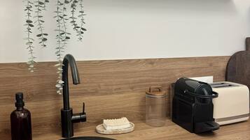 A kitchen with a black sink, a coffee machine, a toaster, a small plant, and a wooden shelf with various items.