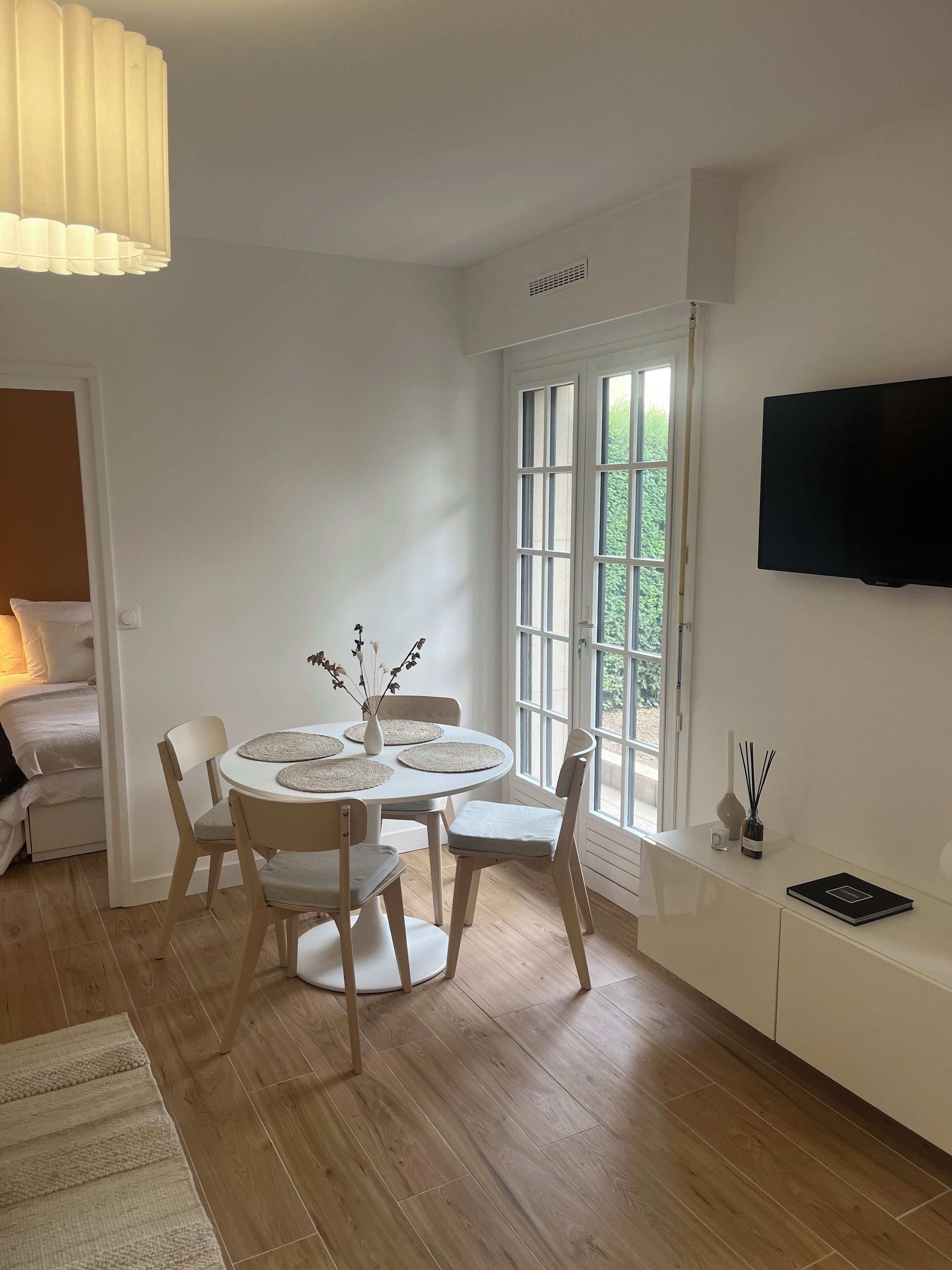 A modern, well-lit room with a dining table, chairs, a sofa, and a TV mounted on the wall.